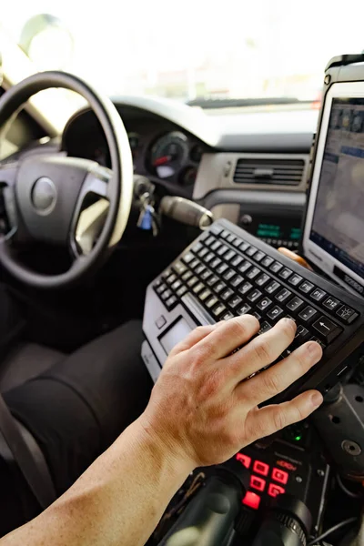 White male police officer hand and fingers typing on keyboard in cop vehicle searching for information to better help make informed decision to pull someone over or not.