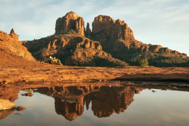 Young couple enjoy a sunset on a rock ledge as the sun sets on cathedral rock in Sedona Arizona USA american southwest with reflection on natural pool at secret slick rock red rock area of yavapai