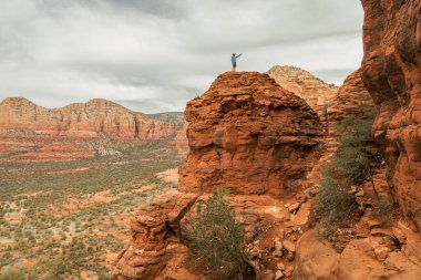 Man hiker standing on Bell Rock with incredible views within coconino national forest in Sedona Arizona USA against white cloud background.