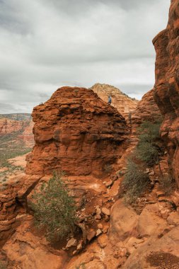 Man hiker standing on Bell Rock with incredible views within coconino national forest in Sedona Arizona USA against white cloud background.