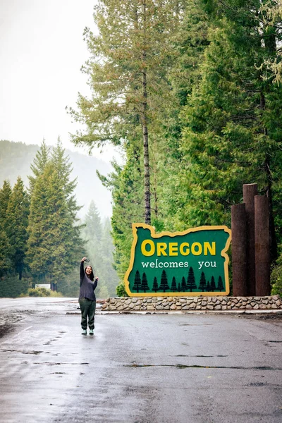 stock image Woman smiles points takes selfie with Oregon welcomes you sign on HWY US-199.