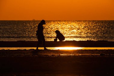 Gün batımında sahilde oynayan insanların silueti.