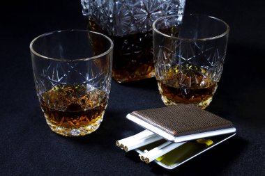 Dekan ve konyaklı bardaklar ve siyah arka planda sigaralı bir sigara tabakası. Yakın plan.