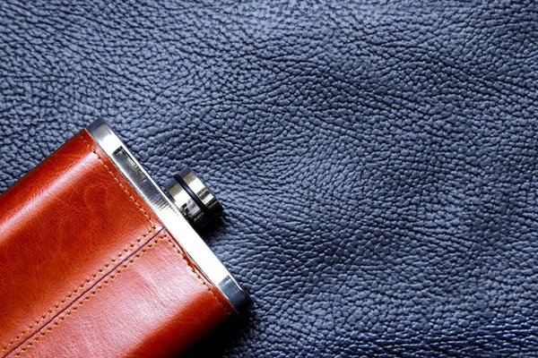 Alcoholic flask in leather trim on the background of black textured leather. Close-up
