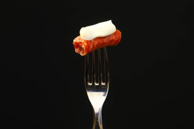 Siyah arka planda çatalda kırılmış bir sosis parçası. Sığ alan derinliği