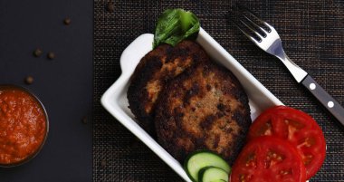 Siyah ışık altında soslu beyaz tabakta sebzeli pirzola. Sığ alan derinliği