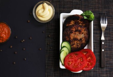 Siyah ışık altında soslu beyaz tabakta sebzeli pirzola. Sığ alan derinliği