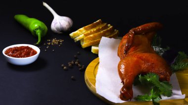 Ekmek ve sebzelerle birlikte karanlık bir yüzeyde kesme tahtasının üzerinde kızarmış tavuk. Yakın plan.