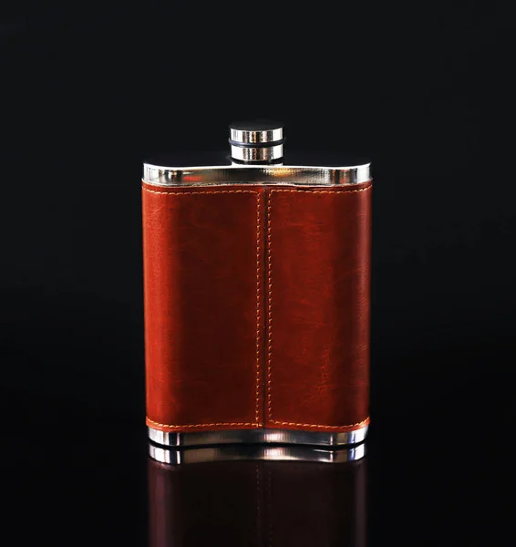 Alcoholic flask in leather trim on a black background with reflection. Close-up