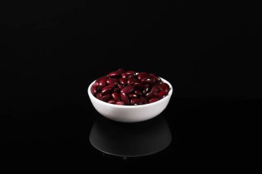 Siyah bir masada beyaz bir tabakta yansımalı fasulye taneleri. Yakın plan.