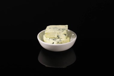 Koyu bir masada üzerinde beyaz bir tabakta mavi küflü Fransız peyniri. Yakın plan.