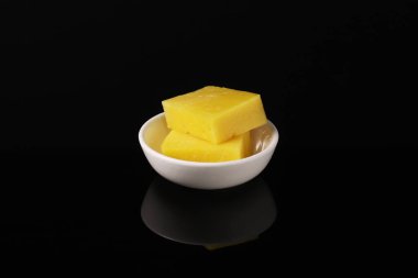 Beyaz tabakta Hollanda peyniri, karanlık bir masada yansımalı. Yakın plan.