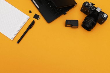 Film kamerası, not defteri ve turuncu arka planda aksiyon kamerası olan foto muhabiri konseptinin en üst görüntüsü. Ofis araçları.
