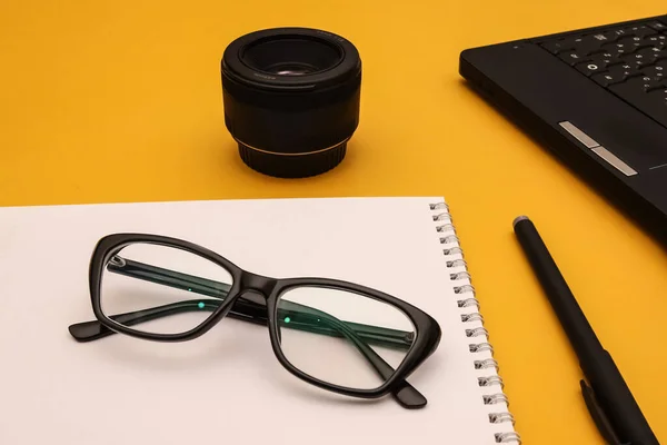 Optical glasses with black frames on the orange desk of a photojournalist. Shallow depth of field