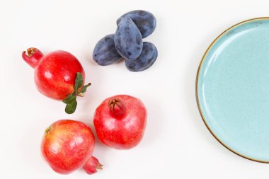 Olgun kırmızı nar ve siyah erik beyaz bir masada. Sığ alan derinliği