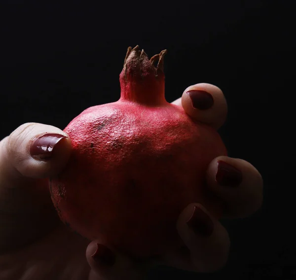 Red ripe pomegranate in a female hand on a black background. Close-up