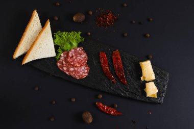 Dilimlenmiş sosis, ekmek, sebze ve diğer malzemelerle birlikte siyah bir stantta. Sığ alan derinliği