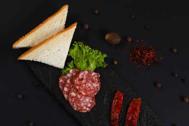 Dilimlenmiş sosis, ekmek, sebze ve diğer malzemelerle birlikte siyah bir stantta. Sığ alan derinliği