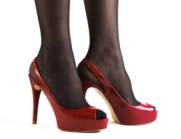 白い背景に赤いハイヒールの靴を持つ暗いストッキングで細い女性の足のペア — ストック写真