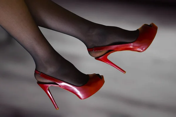 黒のストッキングを着た女性のほっそりとした脚と 赤いハイヒールを背景にした靴のペア — ストック写真