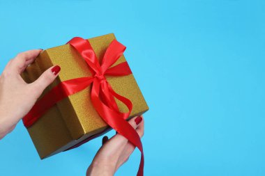 Dişi eller, izole edilmiş mavi arka planda kırmızı kurdeleli altın kraft kağıt hediye kutusunu açıyor.
