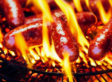 Yangının arka planındaki ızgarada kızarmış sosis. Sığ alan derinliği
