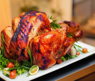 Izgarada kızartılmış hindi, kısmen bir tabakta dilimlenmiş ve festival masasının kenarlarında sebzeler var. Sığ alan derinliği