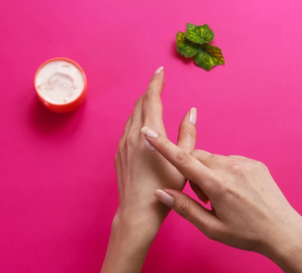 Female hands rub a gentle hand cream on a pink background. Close-up