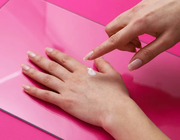 女性の手はピンクの背景に優しいハンドクリームをこすります — ストック写真