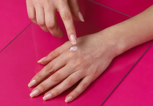 女性の手はピンクの背景に優しいハンドクリームをこすります — ストック写真