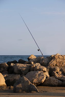 Deniz zeminine karşı deniz taşları arasında bobinli olta. Gün batımında balık tutmak