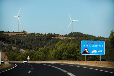 Barselona, İspanya - 10 Temmuz 2024: Dağların tepesinde trafik ışıkları ve rüzgar türbinleriyle İspanya 'da otoyol