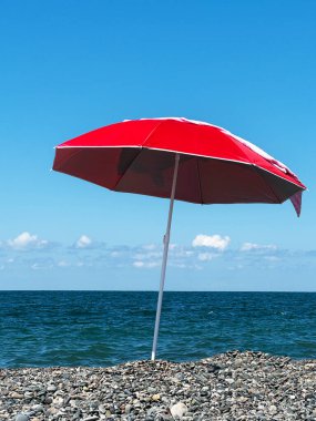 Deniz zeminine karşı deniz taşlarının üzerine yerleştirilmiş kırmızı şemsiye