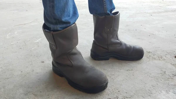 A pair of brown man safety shoes and jeans.