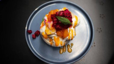 Pavlova serve in a blue plate a meringue dessert usually topped with strawberry and orange fruit and whipped cream.