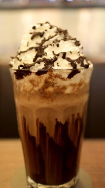 Chocolate milk shake full of cream and melted chocolate in a high glass at the table.