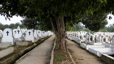 The public cemetery pathway contains identical white ceramic graves at the left and right.