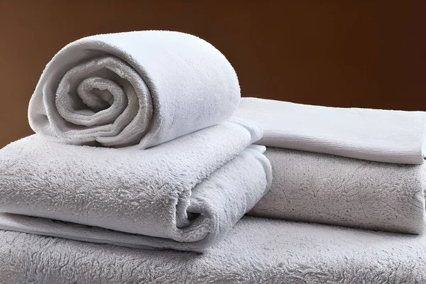 Clean white folded and roll towel nice and tidy stack each other at the table for fitness, bath, swimming, massage and spa marketing background and design material isolated on brown background.