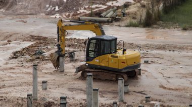 An excavator is working to insert stake or concrete foundation pillars into the ground on a construction site project