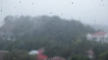 Rain droplets on the window surface glass with hilly nature view bokeh background. Heavy rain outside and the view from indoor apartment.