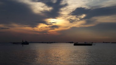 Sanayi bölgesinde günbatımı, mavna silueti, hızlı feribot, büyük lojistik gemi.