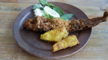 Pecel Lele 'nin ya da Gaga Lele East Java' nın tadını çıkar. Bol yağda kızartılmış kedi balığı, gevrek salatalık, lahana, marul, fesleğen yaprağı, kızarmış tofu ve tempeh ile birlikte. Lezzetli bir Endonezya hoşgörüsü.