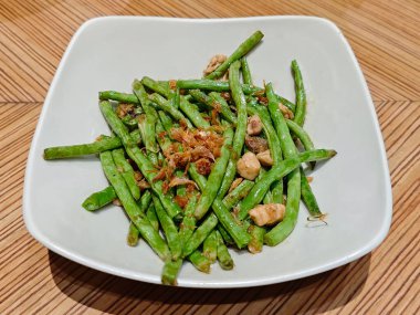 Beyaz tabakta servis edilen kızarmış sarımsaklı yeşil fasulye sebze yemeği..