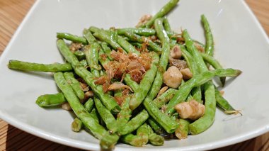 Beyaz tabakta servis edilen kızarmış sarımsaklı yeşil fasulye sebze yemeği..