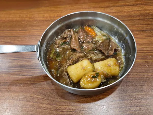 stock image Close Up of Korean Galbi Jjim (Braised Beef Short Ribs) and korean tteokbokki in a Stainless Steel Pan on a Wooden Table