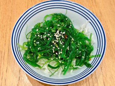 Parlak Yeşil Wakame Salatası Mavi ve Beyaz kâse Tahta Masa üzerinde Susam tohumlu