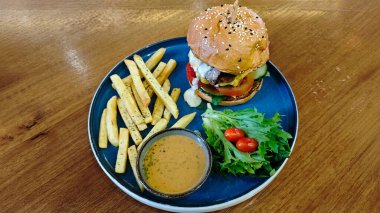 Lezzetli gurme çizburger, patates kızartması, salata ve daldırma soslu, ahşap ahşap masa seti, içinde taze malzemeler ve lezzetli yemekler var.