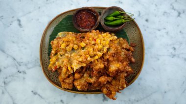 Golden Brown Bakwan Jagung or Indonesian Corn Fritters with Chili Sauce and Fresh Green Chili on Rustic Plate on Marble Table clipart