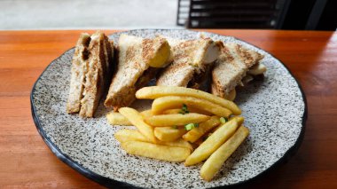 Tavuklu yumurtalı sando sandviçi ve patates kızartması. Doğal ışık altında, benekli tabakta.