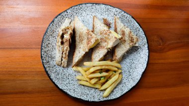 Tavuklu yumurtalı sando sandviçi ve patates kızartması. Doğal ışık altında, benekli tabakta.